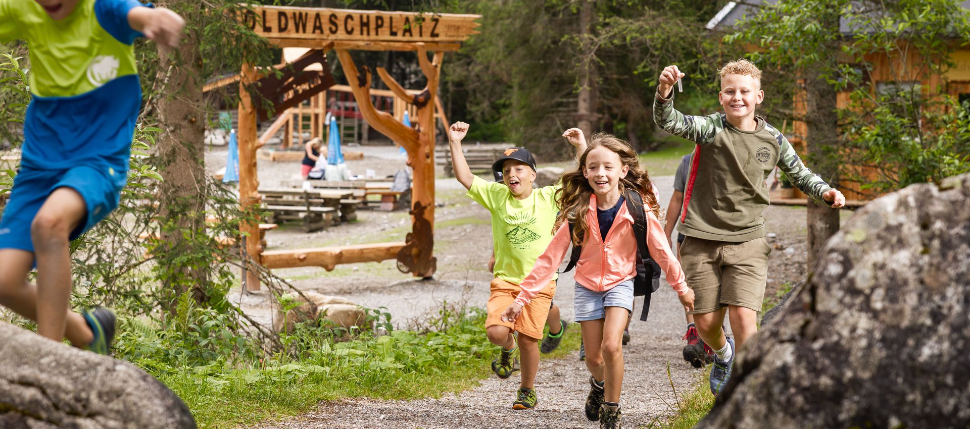 Vier fröhliche Kinder laufen auf Wanderweg im Grünen beim Goldwaschplatz in Rauris