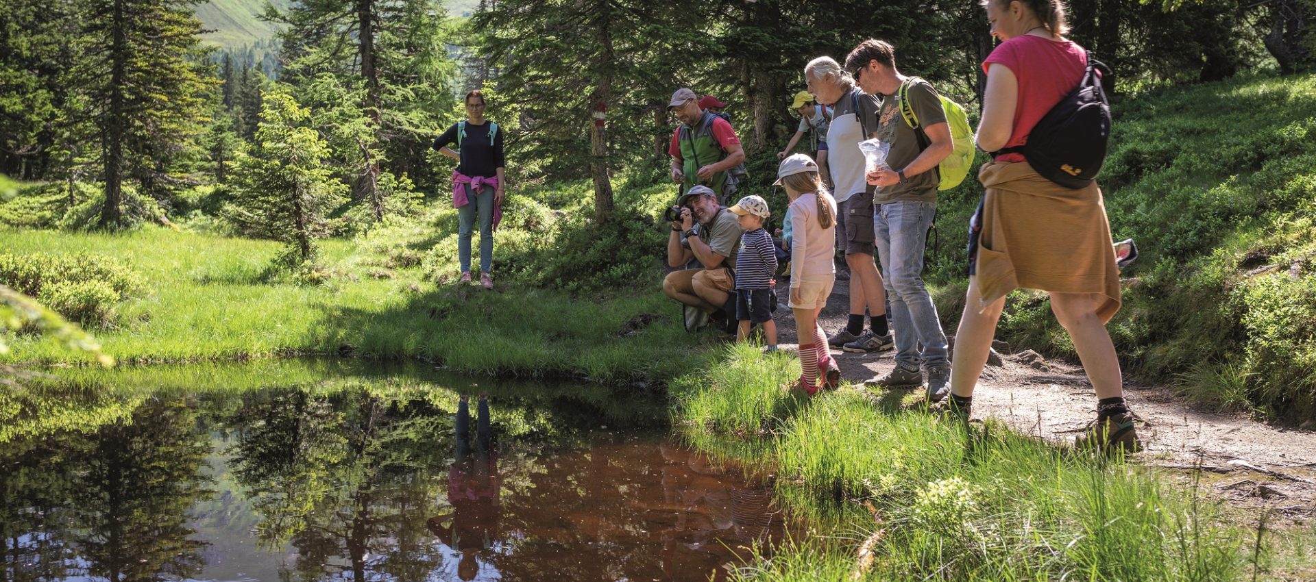 Familiengruppe wandert im Grünen und betrachtet einen kleinen Teich im Raurisertal